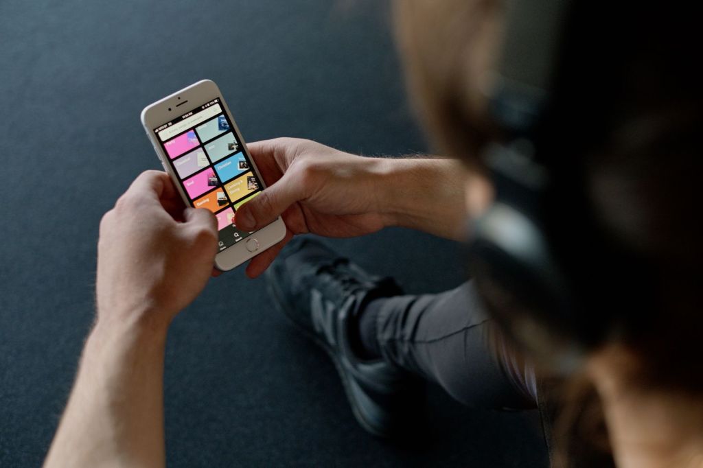 A person wearing headphones scrolls through a music app on a smartphone