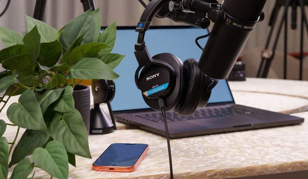 A podcast microphone, headphones, and laptop set up on a desk for recording
