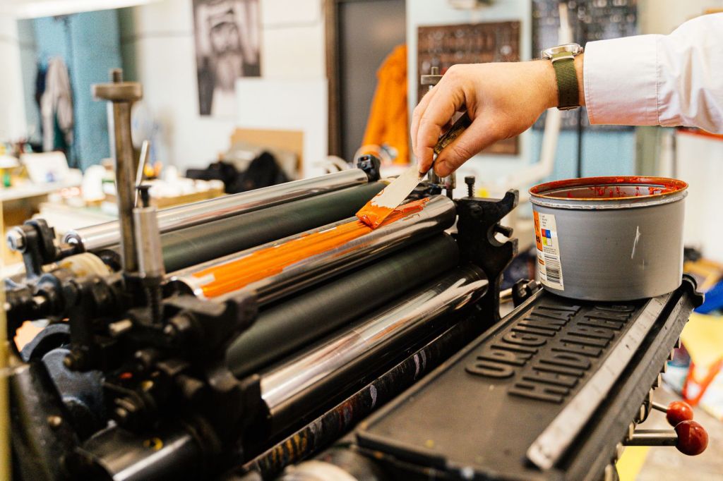 A worker inks the rollers of an old printing press