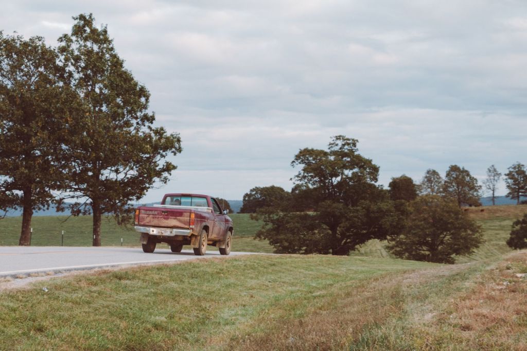 Pickup truck driving on a rural two-lane road past green fields and trees
